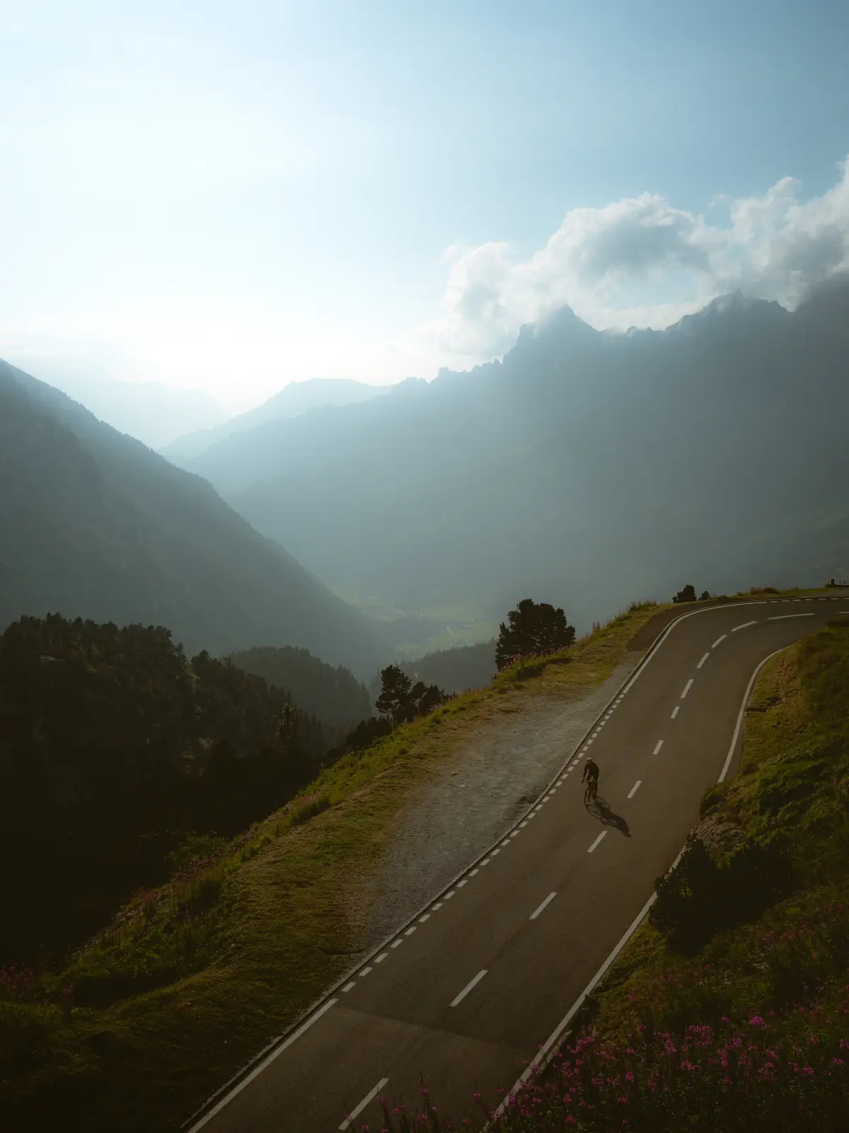 A cyclist rides downhill into a valley in the alps